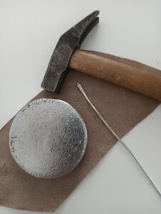 Disco metallico, filo di alluminio, martello e carta abrasiva per realizzare un ciondolo fai da te con materiali di recupero