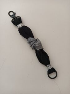 Braccialetto fai da te realizzato con una maglietta riciclata, filo di alluminio e dettaglio decorativo in tessuto grigio