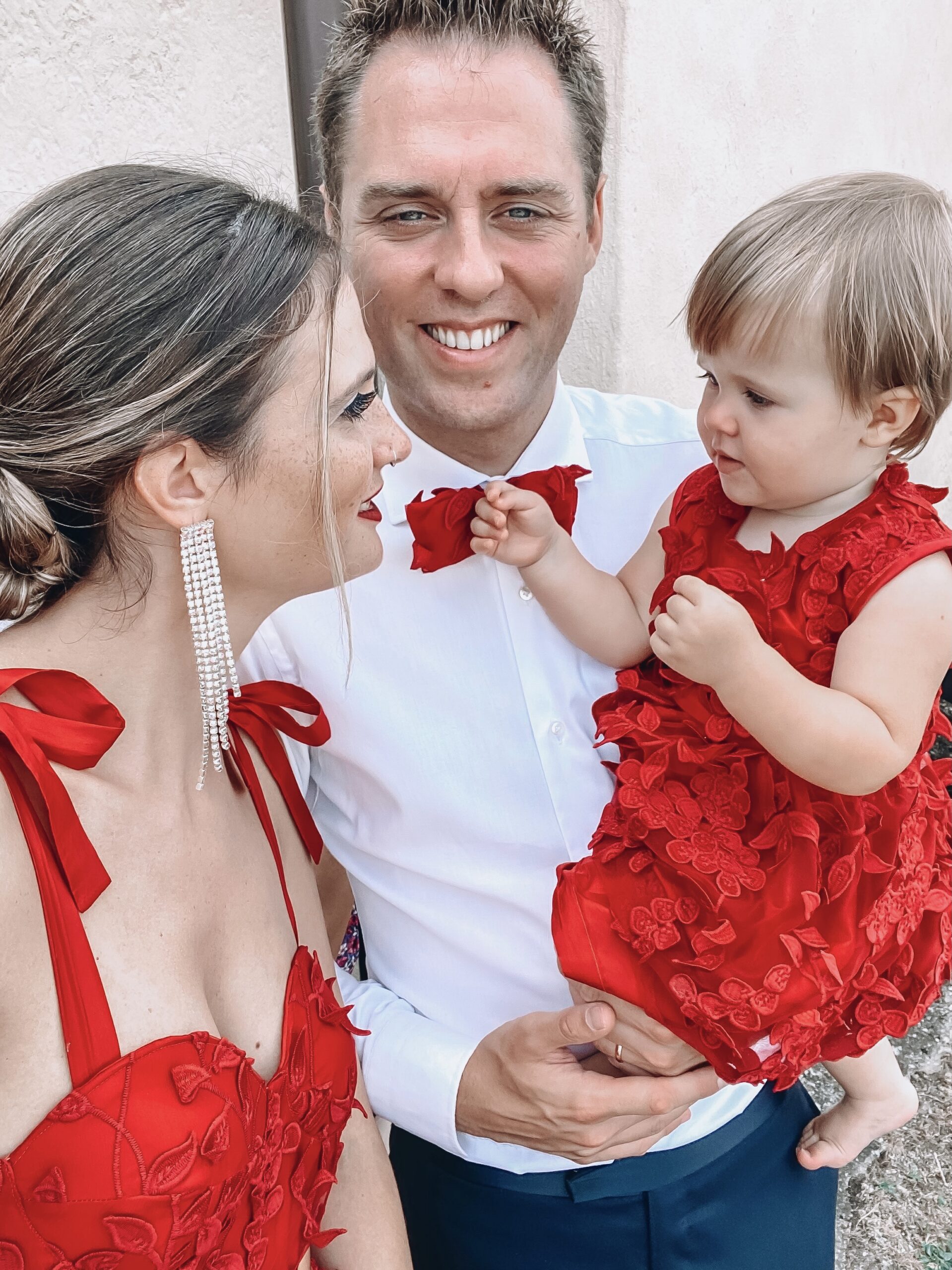 Famiglia composta da madre con il vestito cucito rosso, padre con papillon rosso e bambinacon vestito rosso