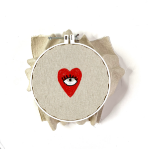occhio dentro cuore rosso con filo rosso infilato in punch needle