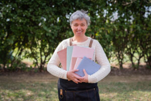 Donna in giardino che sorride con in mano quaderni colorati