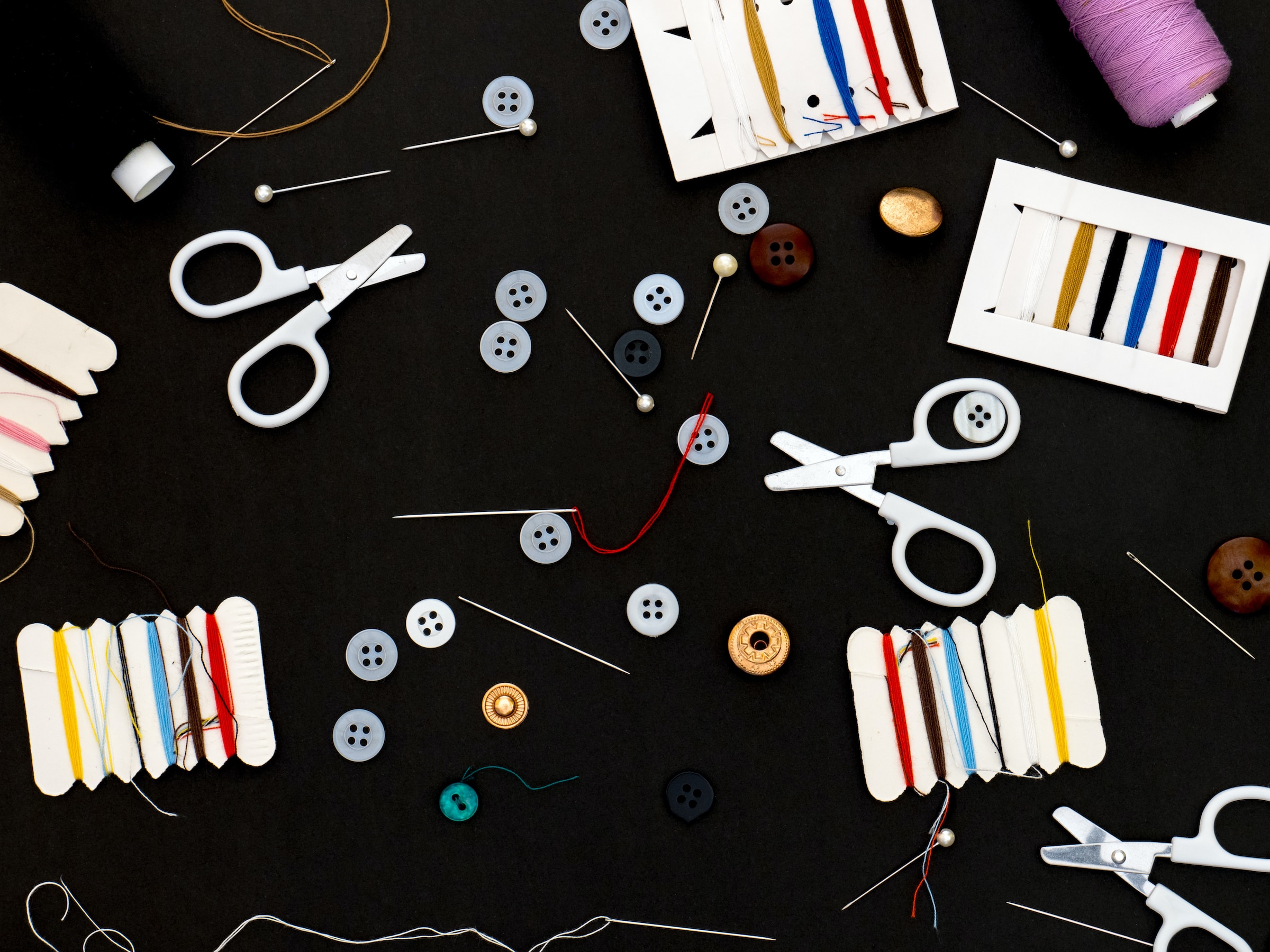 Materiali e strumenti per riparare abiti: forbici, filo, bottoni e aghi