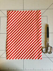 Piano da lavoro con foglio di carta da regalo a strisce bianche e rosse e forbice
