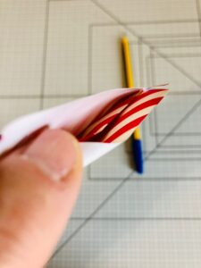 Piano da lavoro con foglio di carta da regalo a strisce bianche e rosse e mano e penne