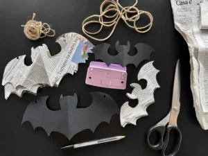 Materiali per realizzare pipistrelli di Halloween in carta di giornale, forbici, penne e spaghi