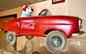 Orso polare di peluche alla guida di una grande automobile giocattolo rossa con logo Coca-Cola
