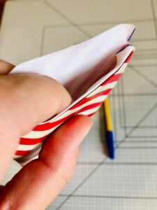 Piano da lavoro con foglio di carta da regalo a strisce bianche e rosse e mano e penna