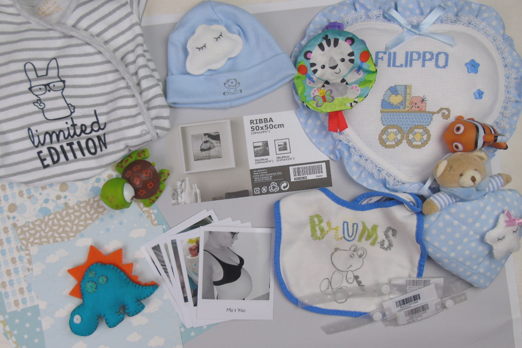 Piano di lavoro con diversi oggetti per neonati: bavaglini, cappellino, foto gravidanza